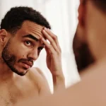 man-inspecting-wrinkles-on-forehead-in-front-of-mirror