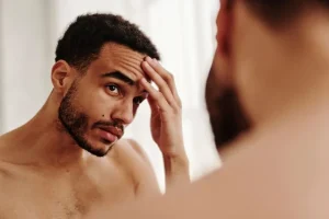 man-inspecting-wrinkles-on-forehead-in-front-of-mirror